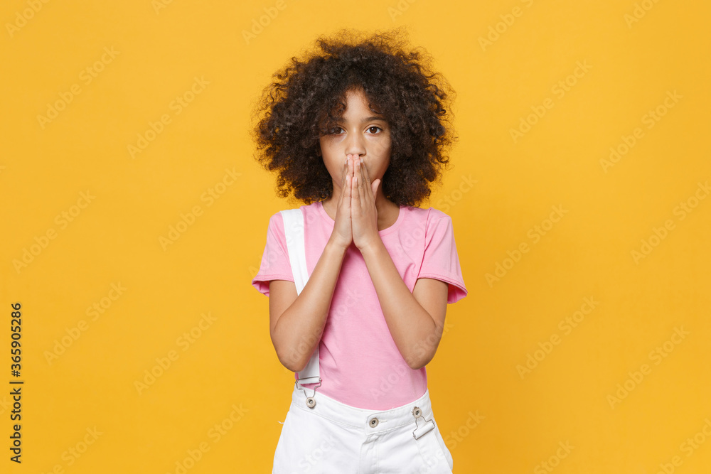 Shocked little african american kid girl 12-13 years old in pink t-shirt isolated on yellow wall background studio portrait. Childhood lifestyle concept. Mock up copy space. Covering mouth with hands. Shocked little african american kid girl 12-13 years old in pink t-shirt isolated on yellow wall background studio portrait. Childhood lifestyle concept. Mock up copy space. Covering mouth with hands.