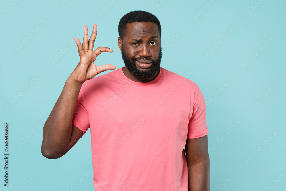 Puzzled young african american man guy in casual pink t-shirt isolated on blue background studio portrait. People lifestyle concept. Mock up copy space. Gesturing demonstrating size with workspace. Puzzled young african american man guy in casual pink t-shirt isolated on blue background studio portrait. People lifestyle concept. Mock up copy space. Gesturing demonstrating size with workspace.