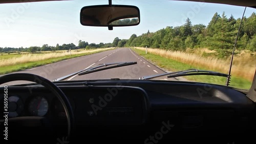 Interior view of an old retro unic AZLK Moskvich 2140 car driving fast at 100 on a new and slim asphalt highway in summer with clear blue sky, sunshine, fields and forest on roadsides photo