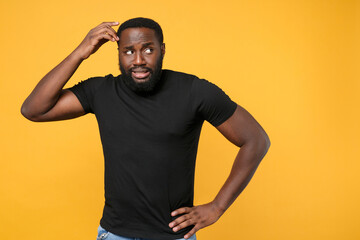 Preoccupied african american man guy football fan in casual black t-shirt isolated on yellow background studio portrait. People lifestyle concept. Mock up copy space. Put hand on head, looking aside.