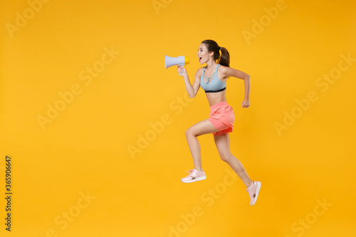 Full length portrait excited young fitness woman in sportswear working out isolated on yellow background. Workout sport motivation lifestyle concept. Mock up copy space. Jump, screaming in megaphone.