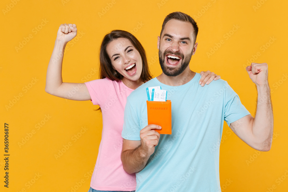 Happy young couple friends guy girl in t-shirts isolated on yellow background. Passenger traveling abroad on weekends getaway. Air flight journey concept. Hold passport tickets, doing winner gesture. Happy young couple friends guy girl in t-shirts isolated on yellow background. Passenger traveling abroad on weekends getaway. Air flight journey concept. Hold passport tickets, doing winner gesture.