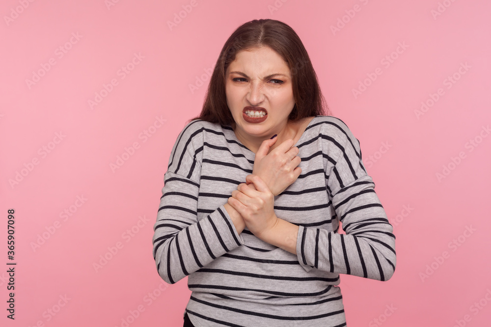 Hand damage, injury. Portrait of woman in striped sweatshirt rubbing sore arm, frowning and suffering from painful sprained wrist, rheumatoid arthritis. indoor studio shot isolated on pink background Hand damage, injury. Portrait of woman in striped sweatshirt rubbing sore arm, frowning and suffering from painful sprained wrist, rheumatoid arthritis. indoor studio shot isolated on pink background