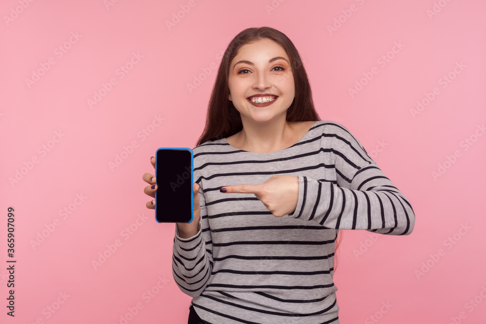 Look at device advertisement! Portrait of happy smiling woman in striped sweatshirt pointing mobile phone with empty display, mock up for app promotion, online web service. indoor studio shot isolated Look at device advertisement! Portrait of happy smiling woman in striped sweatshirt pointing mobile phone with empty display, mock up for app promotion, online web service. indoor studio shot isolated