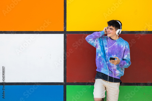 young teenager with cellphone and headphones on the colorful wall