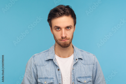 Portrait of unhappy man with bristle in worker denim shirt looking at camera with sad frustrated expression, feeling depressed, upset about troubles. indoor studio shot isolated on blue background © khosrork