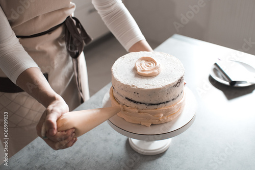 Woman holding pastry bag decorating cake with cream cheese standing in kitchen closeup. Wedding day preparation. photo