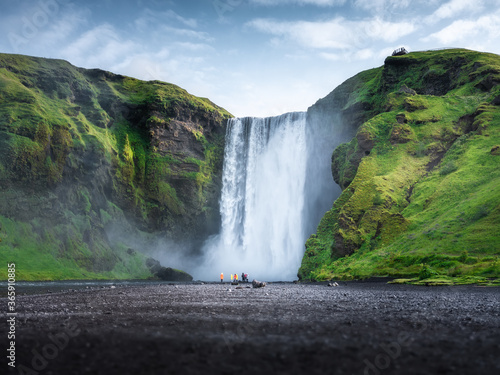 Skogafoss waterfall, Iceland. Mountain valley and clear sky. Natural landscape in summer season. Icelandic nature. Group of a people near large waterfall. Travel image
