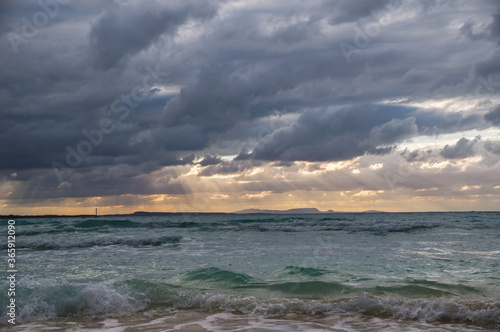 Stormy dark clouds above the sea with sandy beach and curling waves