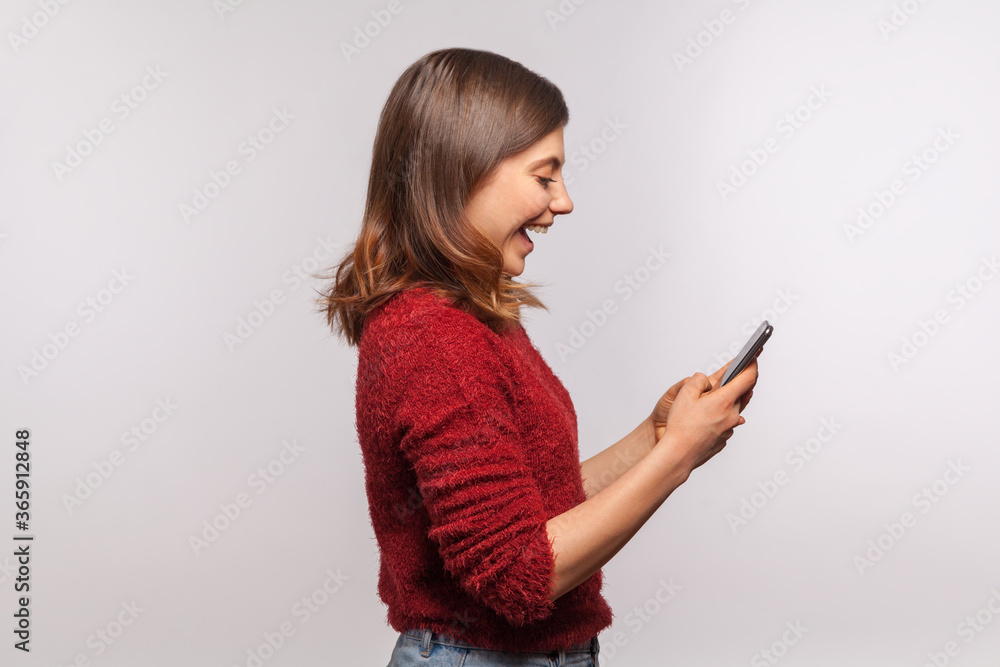 Side view, amazed brunette girl in shaggy sweater using mobile phone with surprised expression, typing or reading shocking message on social network, online communication. studio shot isolated on gray Side view, amazed brunette girl in shaggy sweater using mobile phone with surprised expression, typing or reading shocking message on social network, online communication. studio shot isolated on gray
