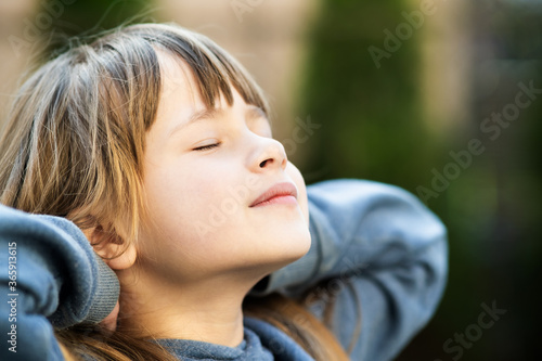 Portrait of young pretty child girl with long hair enjoying warm sunny day in summer outdoors. Cute female kid relaxing on fresh air outside.