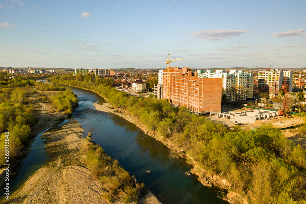 Fototapeta premium Aerial view of tall residential apartment buildings under construction and Bystrytsia river in Ivano-Frankivsk city, Ukraine.