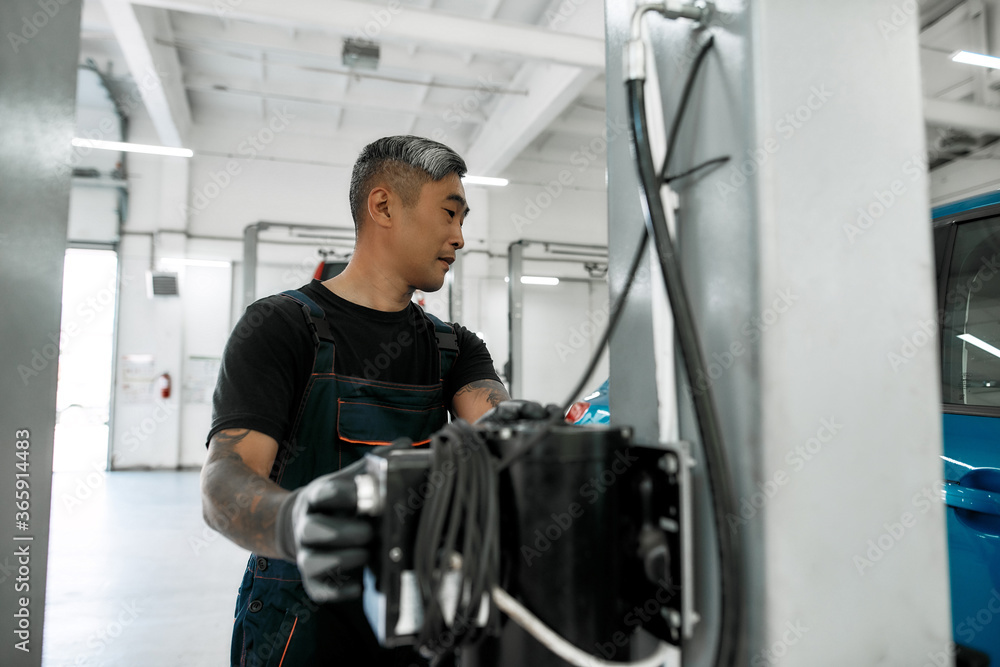 Asian man, professional male mechanic operating hydraulic lift, pushing button up at auto repair shop