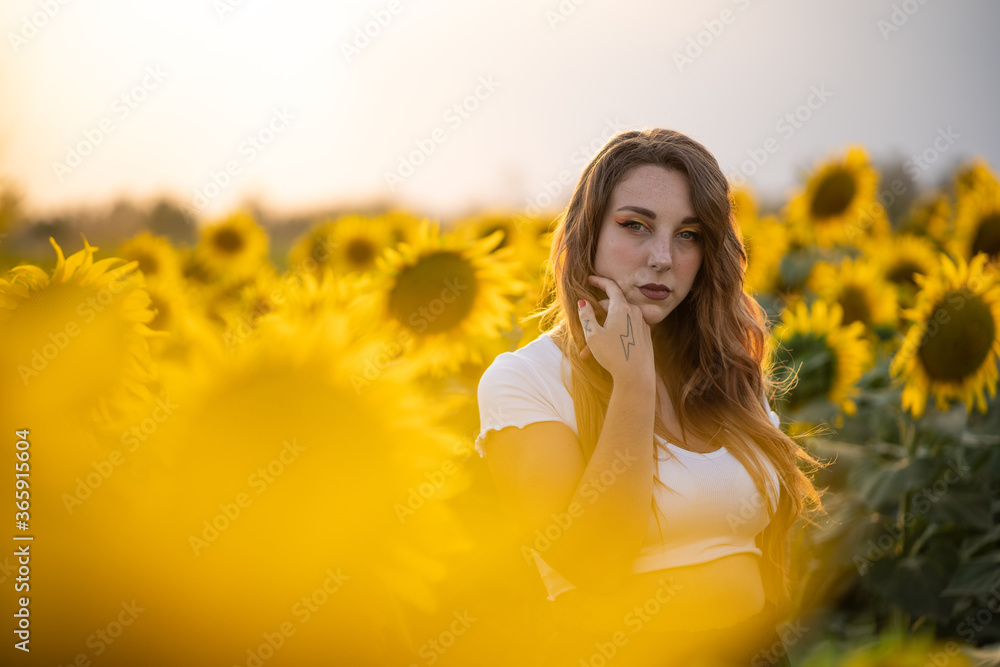 Modelo guapa pelirroja con maquillaje de ojos naranja y amarillo y tatuajes  posando al atardecer en un campo de girasoles en verano, con camiseta  blanca y ojos azules Stock Photo | Adobe