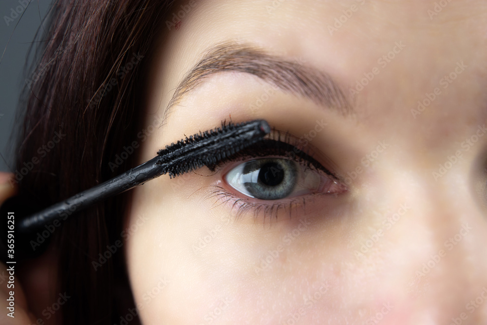 Naklejka premium beautiful girl paints eyes with mascara close-up. cosmetics, personal care