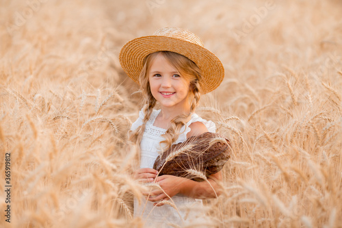 A little blonde girl holds a fresh loaf of bread in a wheat field in the summer. Eco-friendly farm products © КРИСТИНА Игумнова