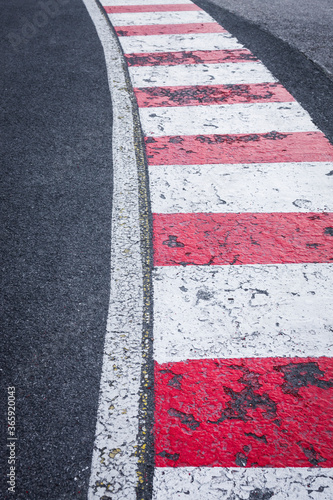 A white line on the right side of asphalt road with red and white painted curbs on the edge. Road turn traffic lines, race course road marking vertical background concept. © YK