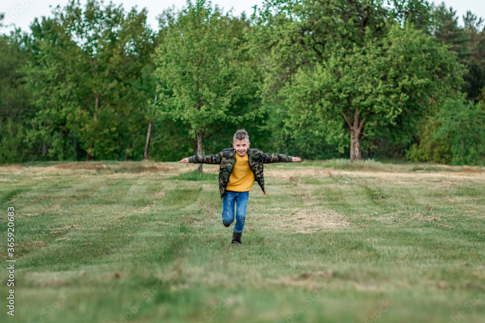 A boy runs across the field with his arms outstretched against a background of greenery. The concept of dreams, choice of profession, pilot, childhood. Copy space. A boy runs across the field with his arms outstretched against a background of greenery. The concept of dreams, choice of profession, pilot, childhood. Copy space.