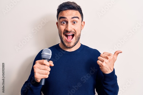 Young handsome singer man with beard singing song using microphone over white background pointing thumb up to the side smiling happy with open mouth