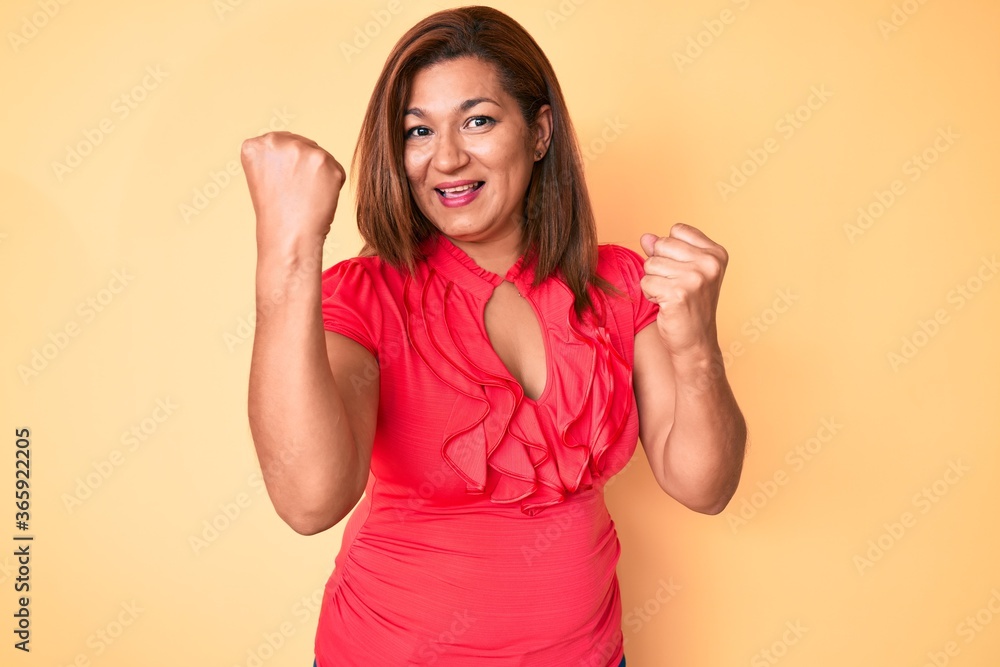 Middle age brunette hispanic woman wearing summer dress screaming proud, celebrating victory and success very excited with raised arms Middle age brunette hispanic woman wearing summer dress screaming proud, celebrating victory and success very excited with raised arms