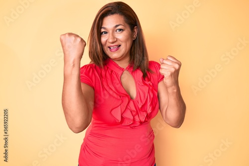 Middle age brunette hispanic woman wearing summer dress screaming proud, celebrating victory and success very excited with raised arms