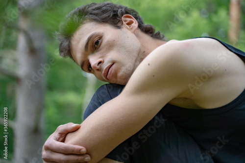 Side view of thoughtful man looking away while hugging knees in forest