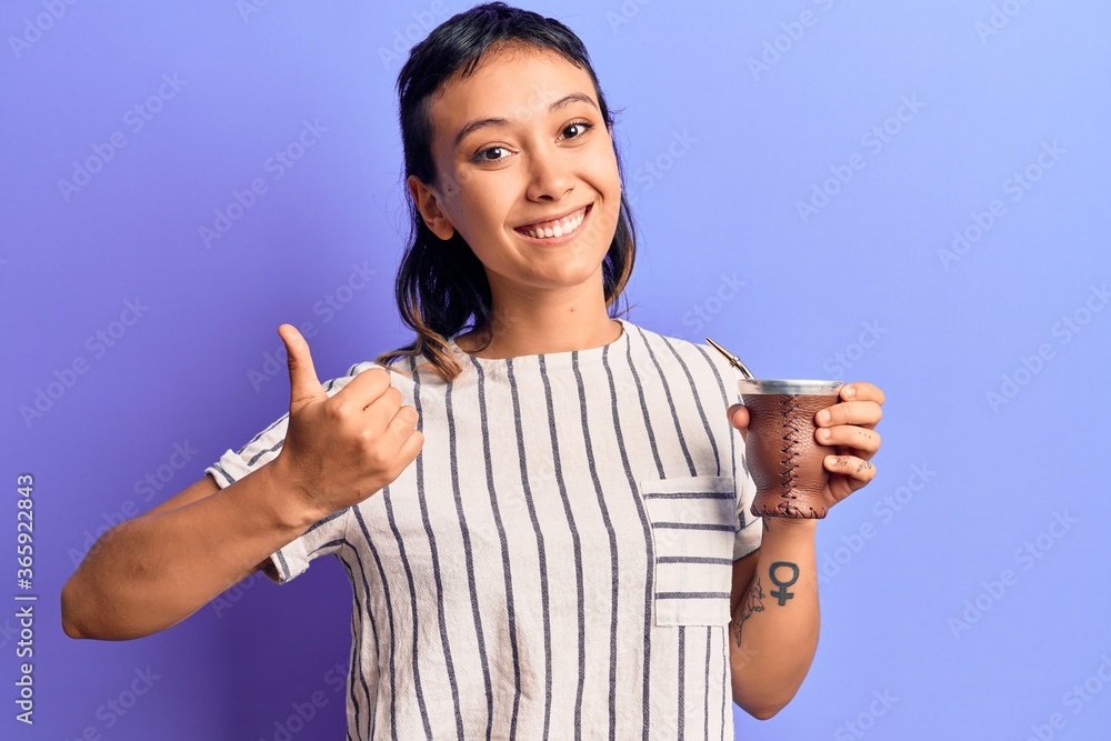 Young woman drinking mate infusion smiling happy and positive, thumb up doing excellent and approval sign Young woman drinking mate infusion smiling happy and positive, thumb up doing excellent and approval sign