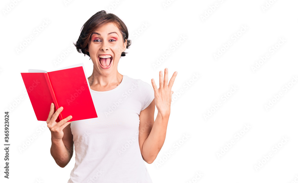 Beautiful young woman with short hair reading a book celebrating victory with happy smile and winner expression with raised hands Beautiful young woman with short hair reading a book celebrating victory with happy smile and winner expression with raised hands