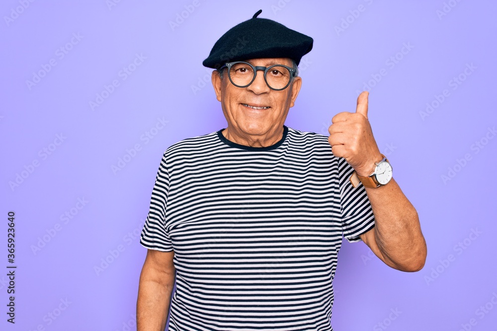 Senior handsome hoary man wearing french beret and glasses standing over purple background doing happy thumbs up gesture with hand. Approving expression looking at the camera showing success. Senior handsome hoary man wearing french beret and glasses standing over purple background doing happy thumbs up gesture with hand. Approving expression looking at the camera showing success.