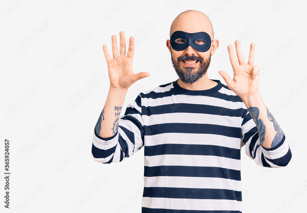 Young handsome man wearing burglar mask showing and pointing up with fingers number nine while smiling confident and happy. Young handsome man wearing burglar mask showing and pointing up with fingers number nine while smiling confident and happy.
