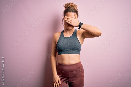 Young beautiful blonde sportswoman doing sport wearing sportswear over pink background covering eyes with hand, looking serious and sad. Sightless, hiding and rejection concept © Krakenimages.com