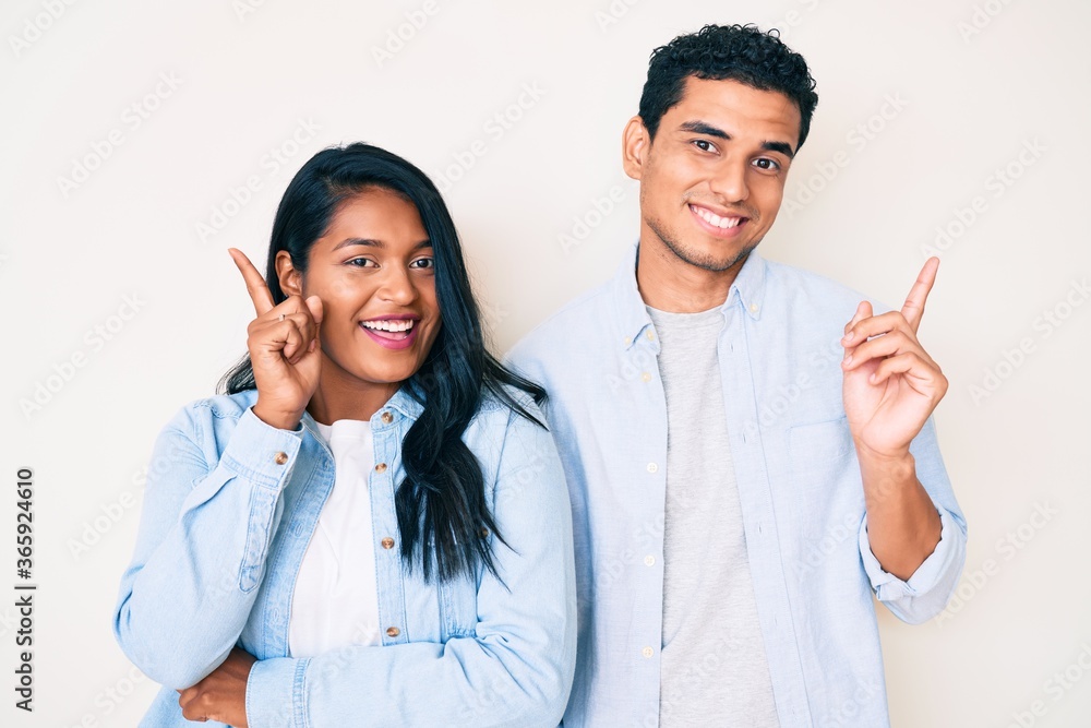 Beautiful latin young couple wearing casual clothes with a big smile on face, pointing with hand and finger to the side looking at the camera. Beautiful latin young couple wearing casual clothes with a big smile on face, pointing with hand and finger to the side looking at the camera.