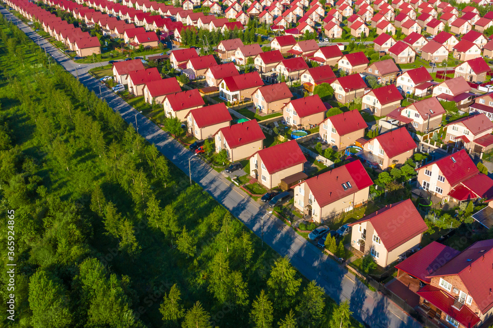 Obraz premium Small houses along the highway. Cottages village. Area is built up with identical cottages. Concept is suburban real estate. Houses with red roofs top view. Country apartments. Taunhaus.