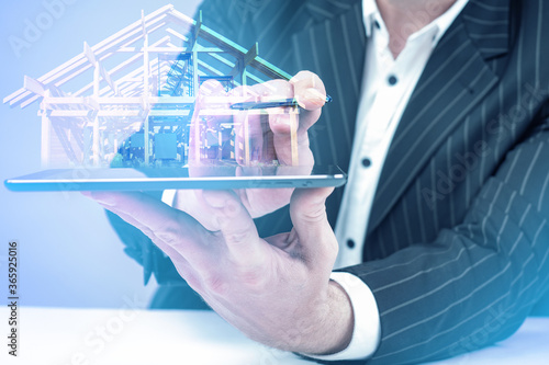Businessman holds home model. Man with tablet in his hands. Model a house next to smartphone. Concept - construction future technology. Construction management technologies. Architectural technology