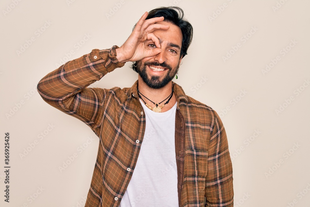 Young handsome hispanic bohemian man wearing hippie style standing over isolated background doing ok gesture with hand smiling, eye looking through fingers with happy face. Young handsome hispanic bohemian man wearing hippie style standing over isolated background doing ok gesture with hand smiling, eye looking through fingers with happy face.