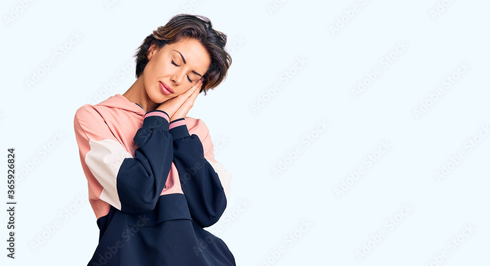 Young beautiful woman wearing sportswear sleeping tired dreaming and posing with hands together while smiling with closed eyes. Young beautiful woman wearing sportswear sleeping tired dreaming and posing with hands together while smiling with closed eyes.