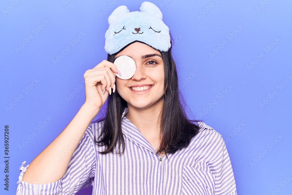 Young beautiful girl wearing funny sleep mask using makeup remover cotton looking positive and happy standing and smiling with a confident smile showing teeth Young beautiful girl wearing funny sleep mask using makeup remover cotton looking positive and happy standing and smiling with a confident smile showing teeth