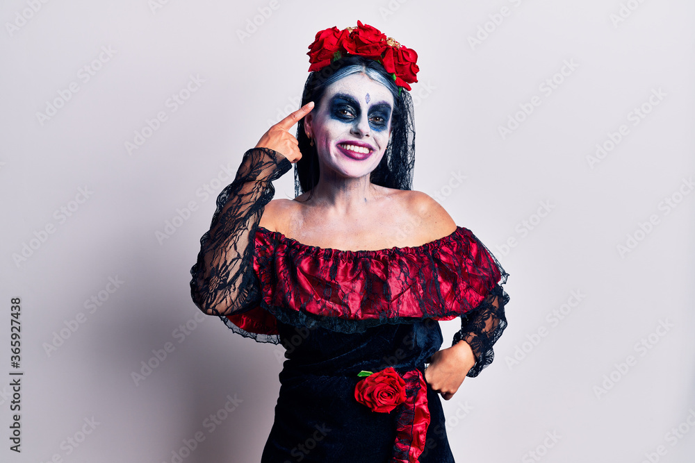 Young woman wearing mexican day of the dead makeup smiling pointing to head with one finger, great idea or thought, good memory Young woman wearing mexican day of the dead makeup smiling pointing to head with one finger, great idea or thought, good memory