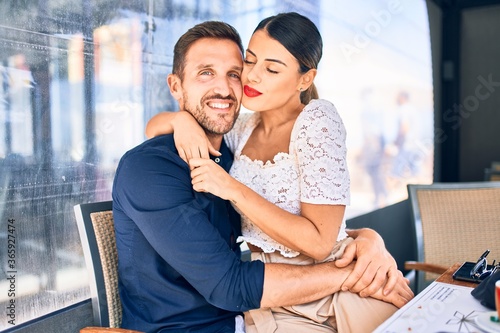 Young beautiful couple smiling happy and confident. Sitting with smile on face hugging at restaurant.