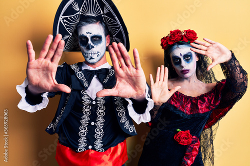 Young couple wearing mexican day of the dead costume over yellow doing frame using hands palms and fingers, camera perspective