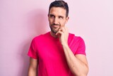 Young handsome man wearing casual t-shirt standing over isolated pink background thinking concentrated about doubt with finger on chin and looking up wondering