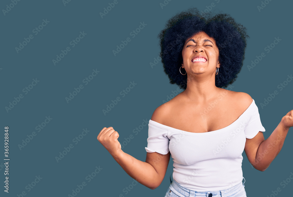 Young african american girl wearing casual clothes very happy and excited doing winner gesture with arms raised, smiling and screaming for success. celebration concept. Young african american girl wearing casual clothes very happy and excited doing winner gesture with arms raised, smiling and screaming for success. celebration concept.