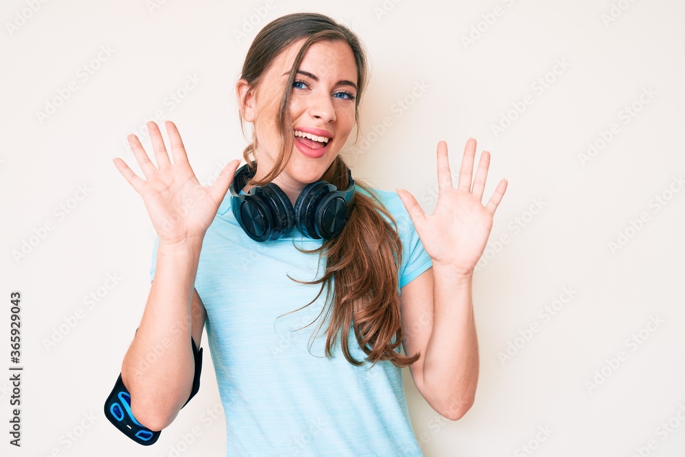 Beautiful young caucasian woman wearing gym clothes and using headphones showing and pointing up with fingers number ten while smiling confident and happy. Beautiful young caucasian woman wearing gym clothes and using headphones showing and pointing up with fingers number ten while smiling confident and happy.