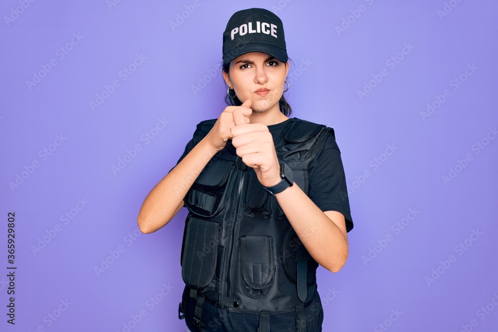 Young police woman wearing security bulletproof vest uniform over purple background Ready to fight with fist defense gesture, angry and upset face, afraid of problem Young police woman wearing security bulletproof vest uniform over purple background Ready to fight with fist defense gesture, angry and upset face, afraid of problem