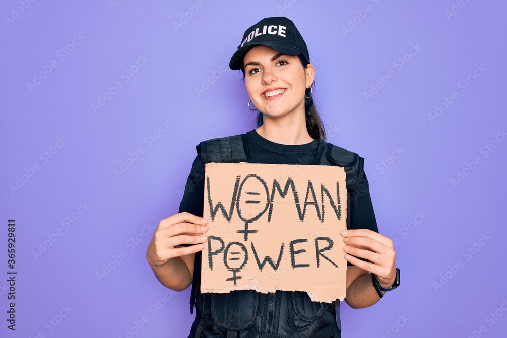 Police woman wearing security bulletproof vest uniform holding woman power protest cardboard with a happy face standing and smiling with a confident smile showing teeth Police woman wearing security bulletproof vest uniform holding woman power protest cardboard with a happy face standing and smiling with a confident smile showing teeth