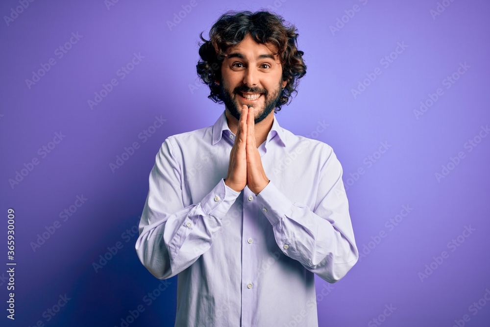 Young handsome business man with beard wearing shirt standing over purple background praying with hands together asking for forgiveness smiling confident. Young handsome business man with beard wearing shirt standing over purple background praying with hands together asking for forgiveness smiling confident.
