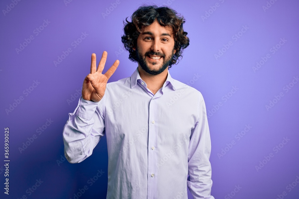 Naklejka premium Young handsome business man with beard wearing shirt standing over purple background showing and pointing up with fingers number three while smiling confident and happy.