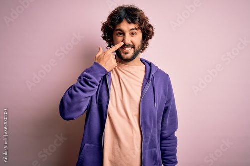 Young handsome sporty man with beard wearing casual sweatshirt over pink background Pointing with hand finger to face and nose, smiling cheerful. Beauty concept © Krakenimages.com