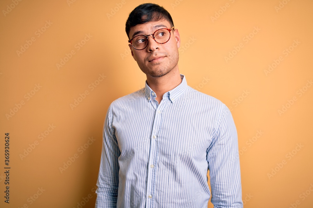 Young handsome hispanic business man wearing nerd glasses over yellow background smiling looking to the side and staring away thinking. Young handsome hispanic business man wearing nerd glasses over yellow background smiling looking to the side and staring away thinking.
