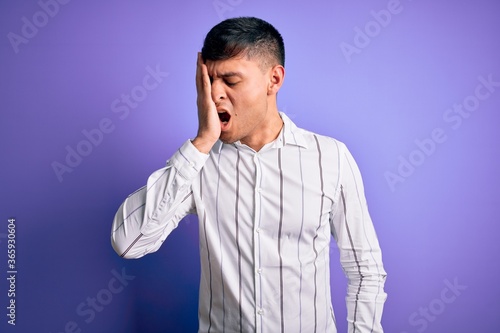 Young handsome hispanic man wearing elegant business shirt standing over purple background Yawning tired covering half face, eye and mouth with hand. Face hurts in pain.